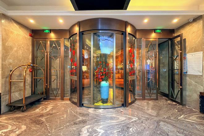 A revolving door with a glass enclosure, a marble floor, and a blue vase in the center.