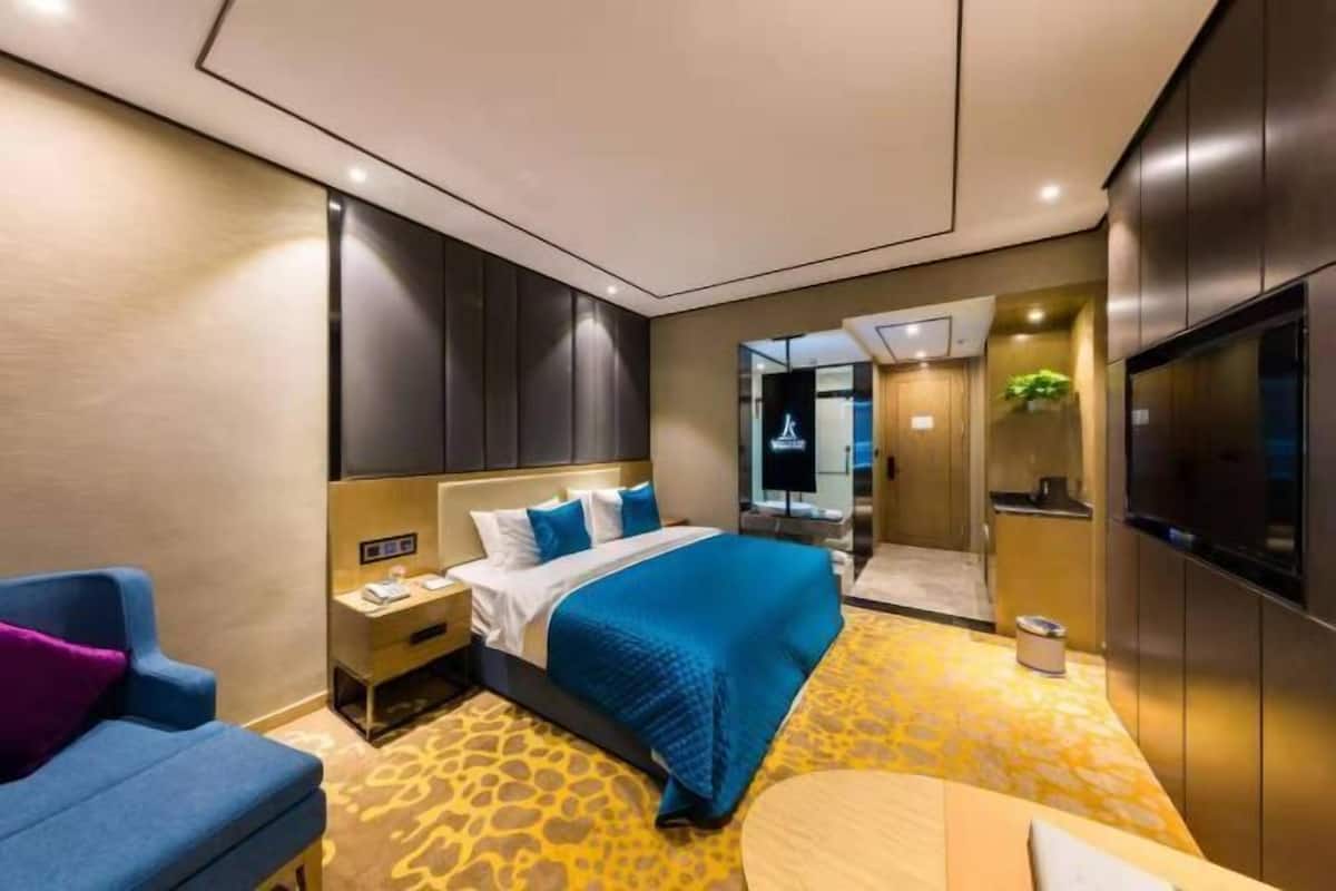 A modern hotel room with a large bed, a desk, a chair, and a television.