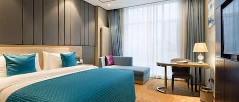 Quarto de hotel com cama, escrivaninha, cadeira, sofá e televisão.