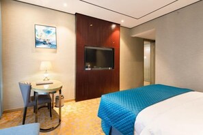 A hotel room with a bed, a desk with a chair, a television, and a painting on the wall. - Kaibin International Hotel (Xining)