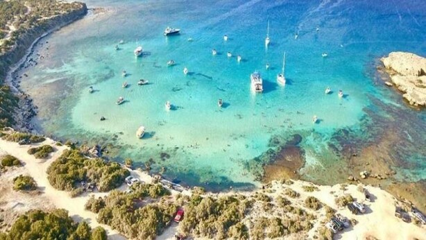 An aerial view of a coastal area with clear turquoise waters, boats, and a sandy beach.