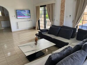 A modern living room with a sectional sofa, a flat-screen TV, and a large window with curtains.