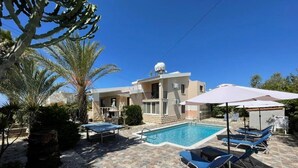 A pool area with lounge chairs, a stone-tiled deck, and a building with a satellite dish.
