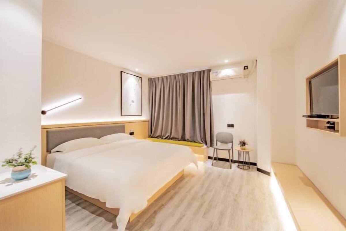 A modern hotel room with a bed, bedside table, and a small seating area with a chair and table.