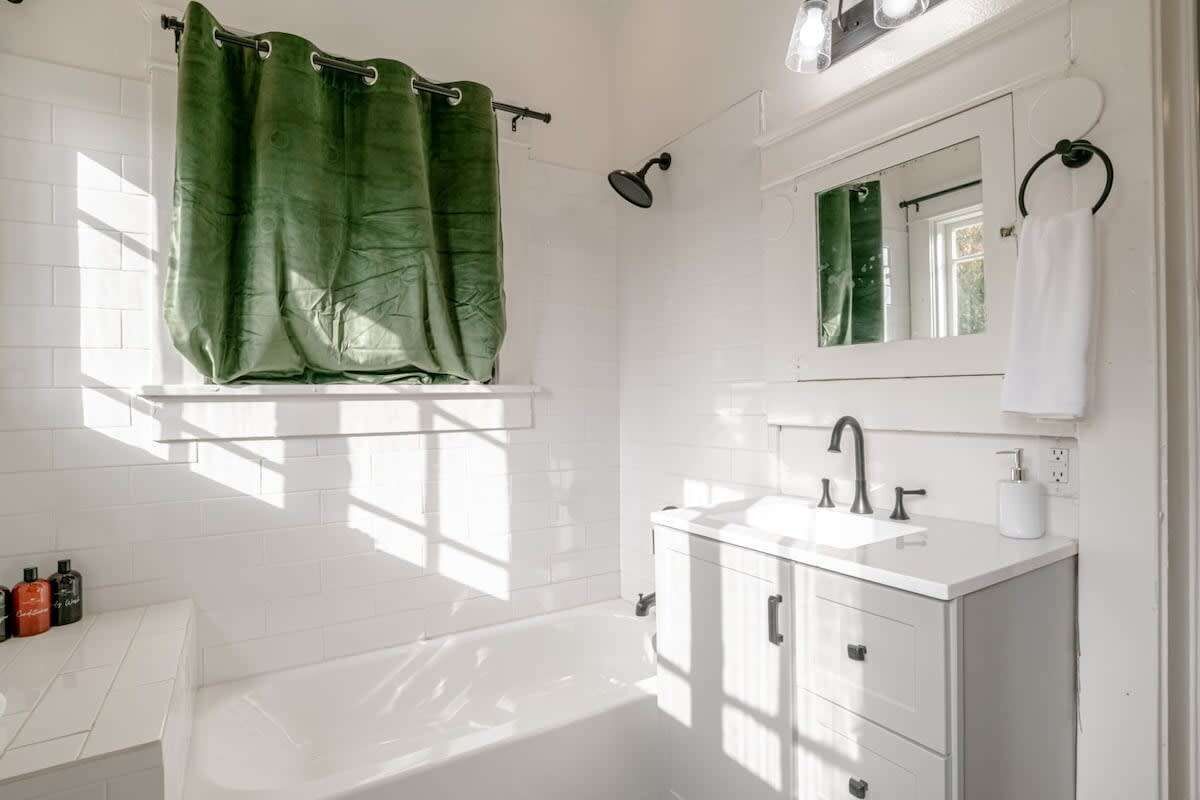 Ein Badezimmer mit einer weißen Badewanne, einem Waschtisch mit Spiegel und einem grünen Duschvorhang.