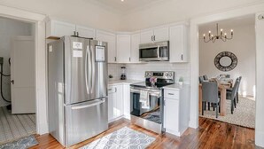 Una cocina moderna con electrodomésticos de acero inoxidable, armarios blancos y una zona de comedor con candelabro.