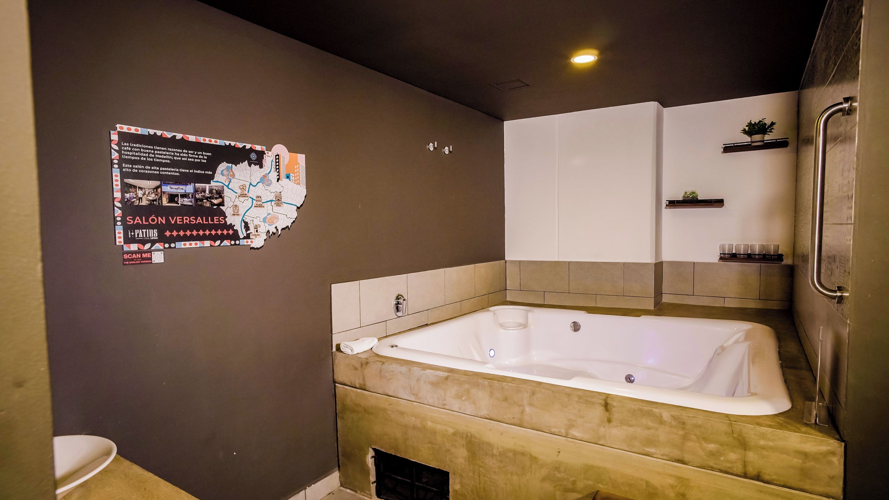 Une salle de bain moderne avec une grande baignoire, des toilettes et un espace douche. Un poster est affiché sur le mur, faisant la publicité d’une entreprise locale.