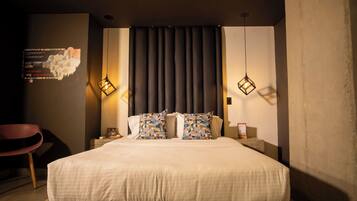 Una habitación de hotel moderna con una cama grande, almohadas con estampado geométrico, un cabecero oscuro y lámparas colgantes.