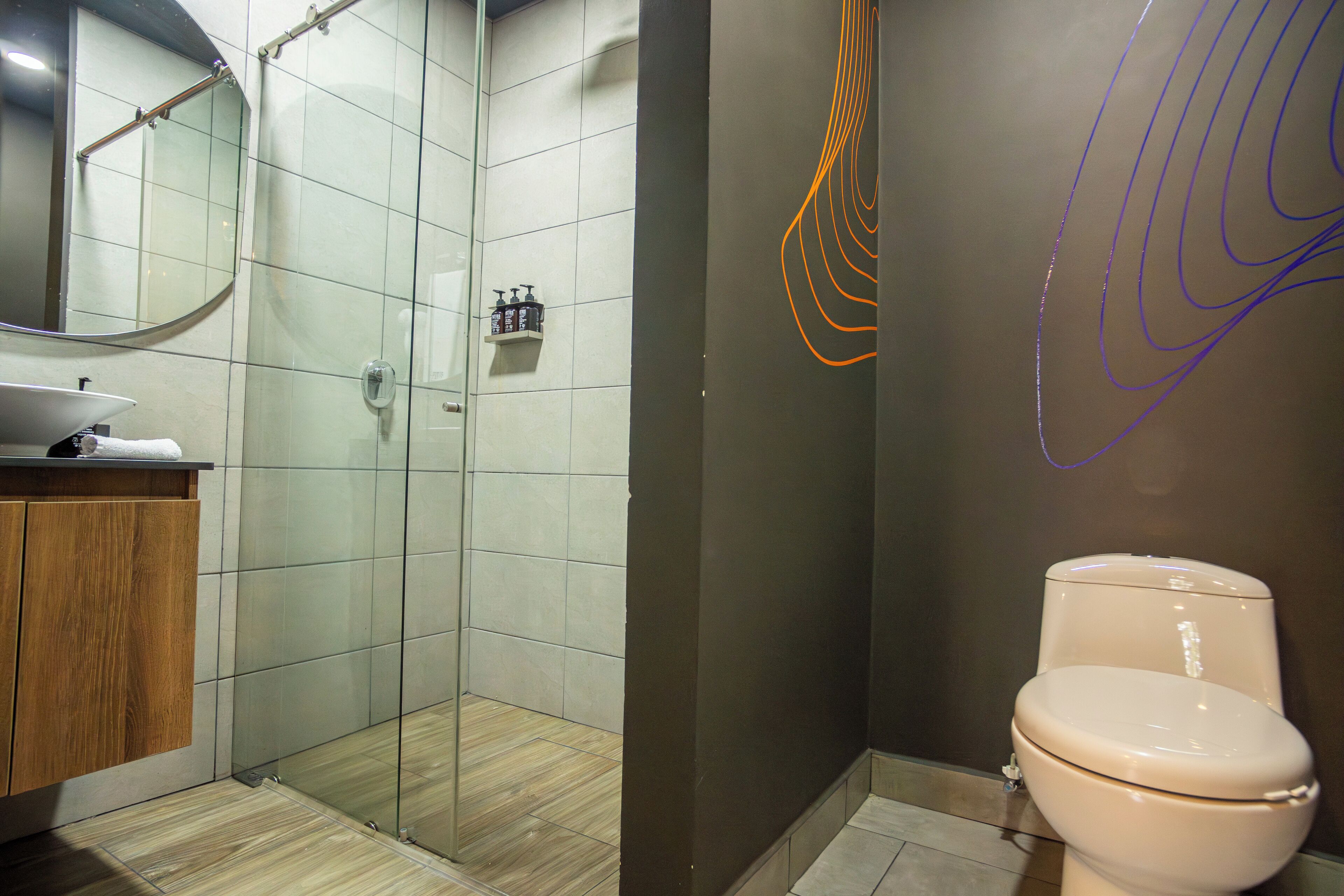 A bathroom with a glass shower enclosure, a toilet, and a sink with a mirror above it.