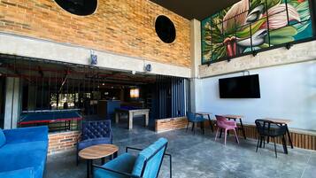 A spacious indoor area with a brick wall, a pool table, and various seating options including blue and pink chairs.