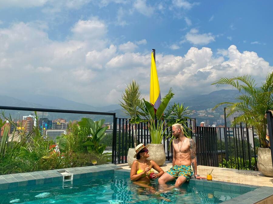A rooftop pool with clear blue water, surrounded by lush greenery and a cityscape view.