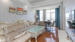 A living room with a sofa, coffee table, and TV. There are three paintings on the wall. - Jinghe Holiday Hotel (Wuhan)