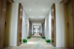 A long, narrow hallway with wooden doors on both sides, potted plants along the center, and a carpeted floor. - Jinghe Holiday Hotel (Wuhan)
