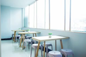 A classroom with tables and stools arranged in rows, large windows, and a view outside. - Jinghe Holiday Hotel (Wuhan)