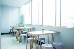 Un aula con mesas y taburetes dispuestos en filas, amplias ventanas y vistas al exterior.