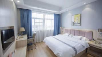 Habitación de hotel con cama, escritorio, silla, televisor y ventana con cortinas.