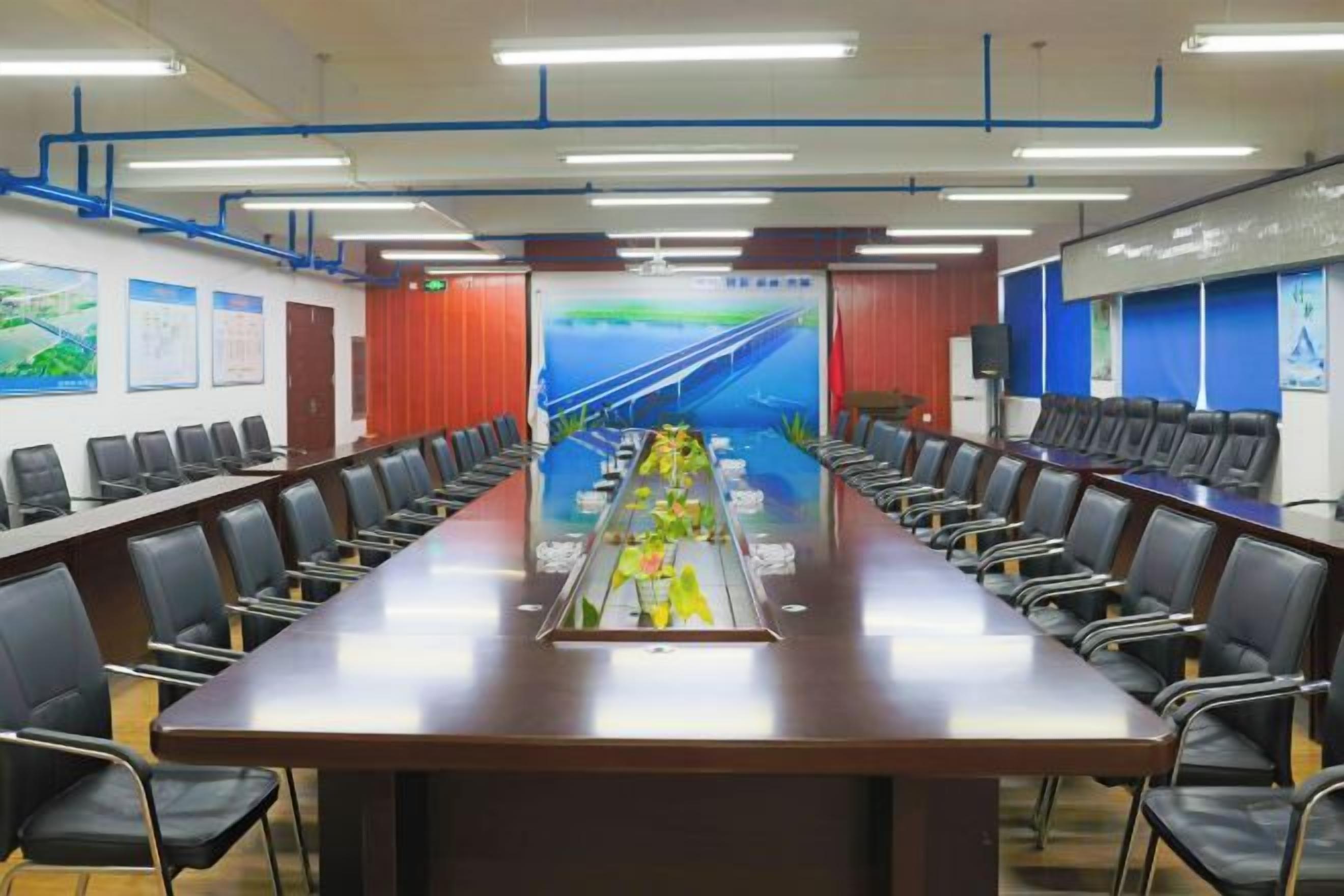 Una sala de conferencias con una larga mesa, sillas y una pantalla de proyector.