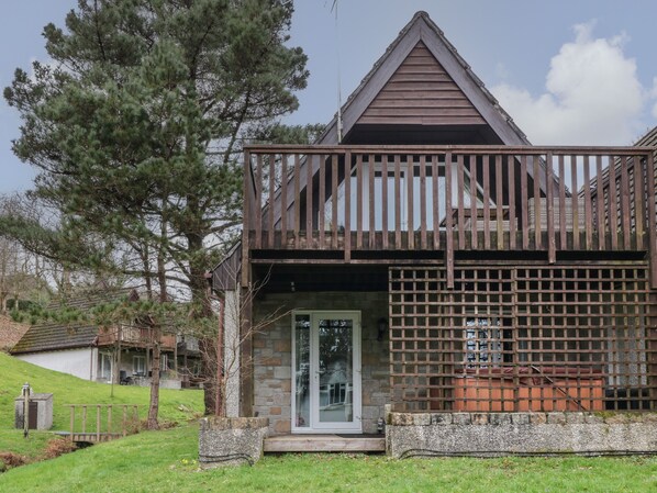 A two-story wooden cabin with a balcony, stone foundation, and a small porch area. - Valley Lodge 33 (Gunnislake)