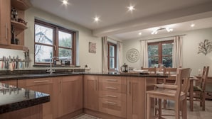 Une cuisine moderne avec des meubles en bois, un plan de travail en granit et un coin repas comprenant des chaises et une table en bois.