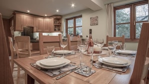 Un coin repas avec des meubles en bois, une table dressée pour quatre personnes et une cuisine en arrière-plan.