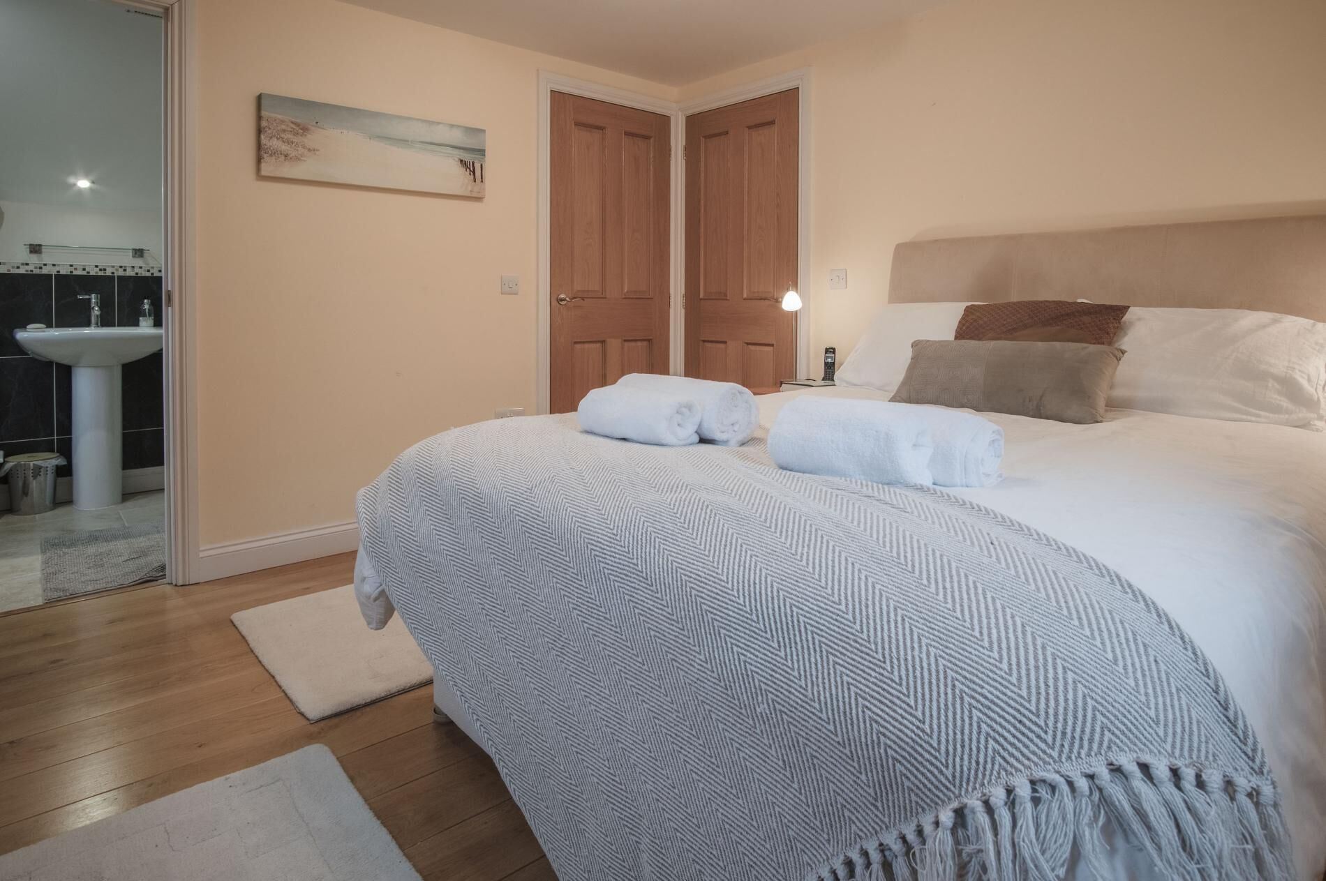 A bedroom with a large bed, two doors, a bedside table with a lamp, and a painting on the wall.