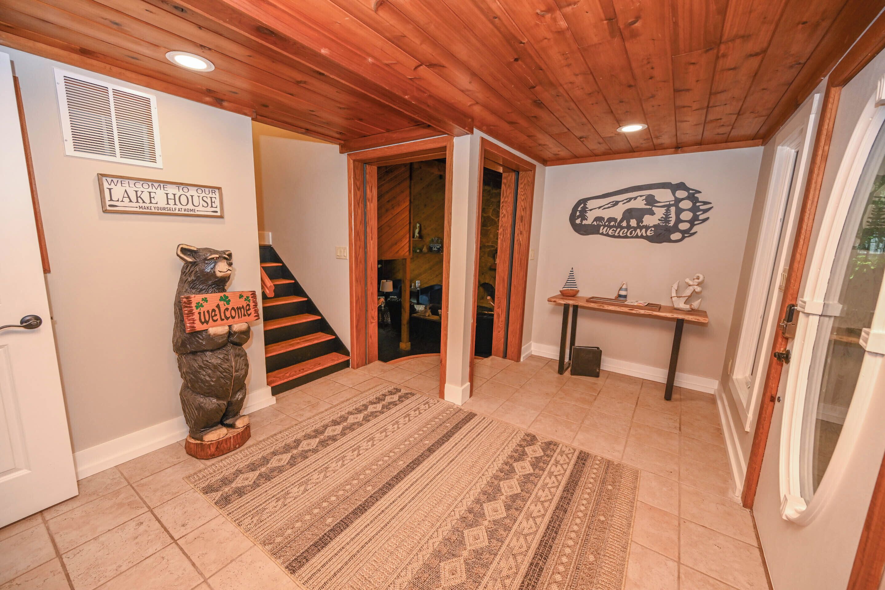 A wooden interior with a welcome sign, a bear statue, a staircase, and a wall decal.