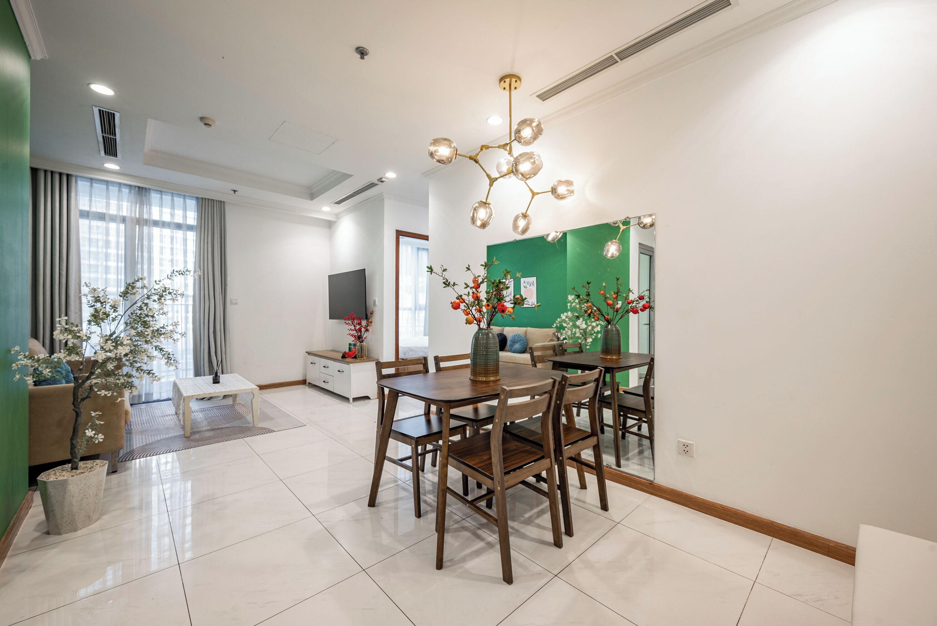 A modern living room with a dining area, a green accent wall, and a decorative chandelier.