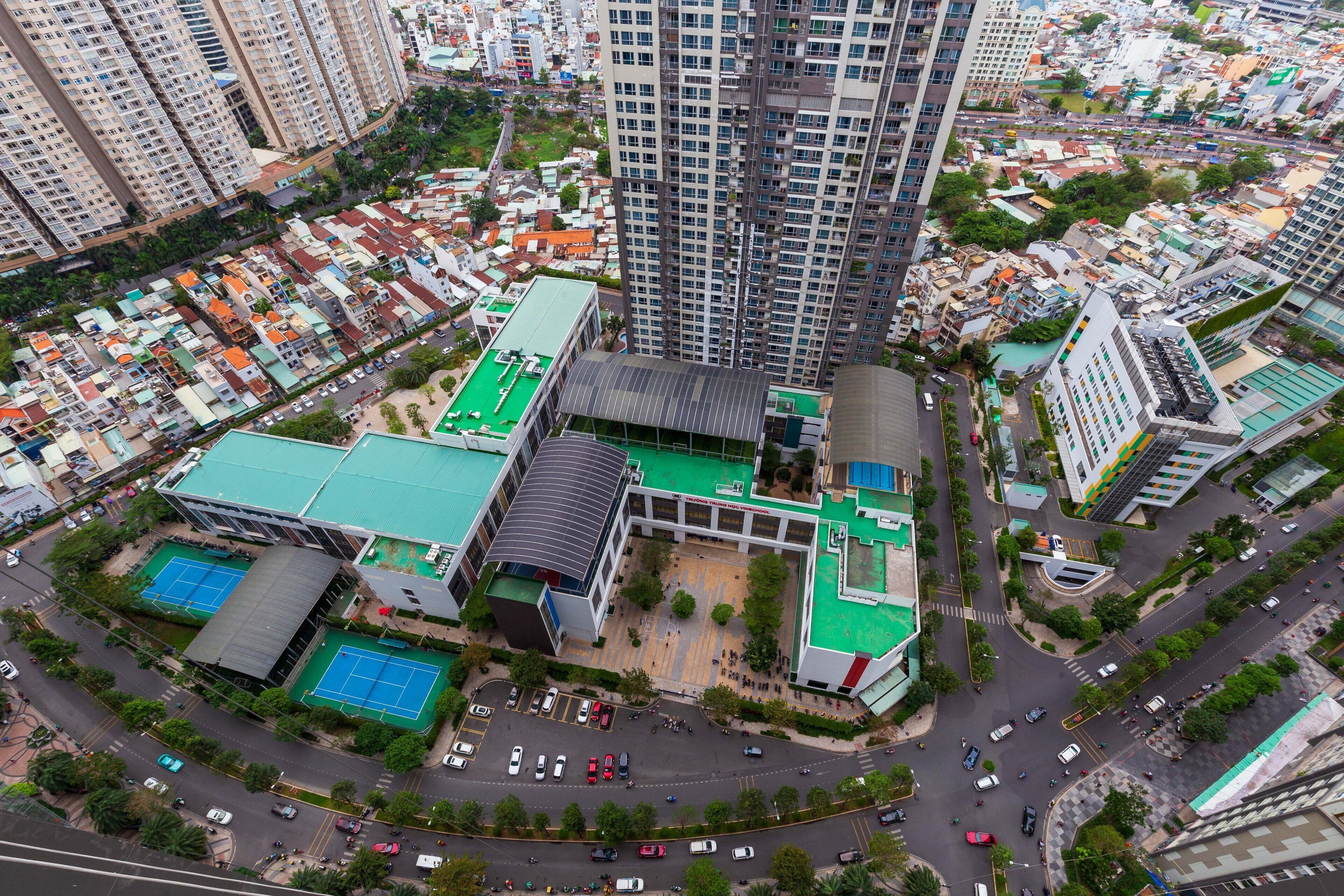 An aerial view of a modern building complex with multiple high-rise residential towers, a central courtyard with tennis courts, and a parking area.