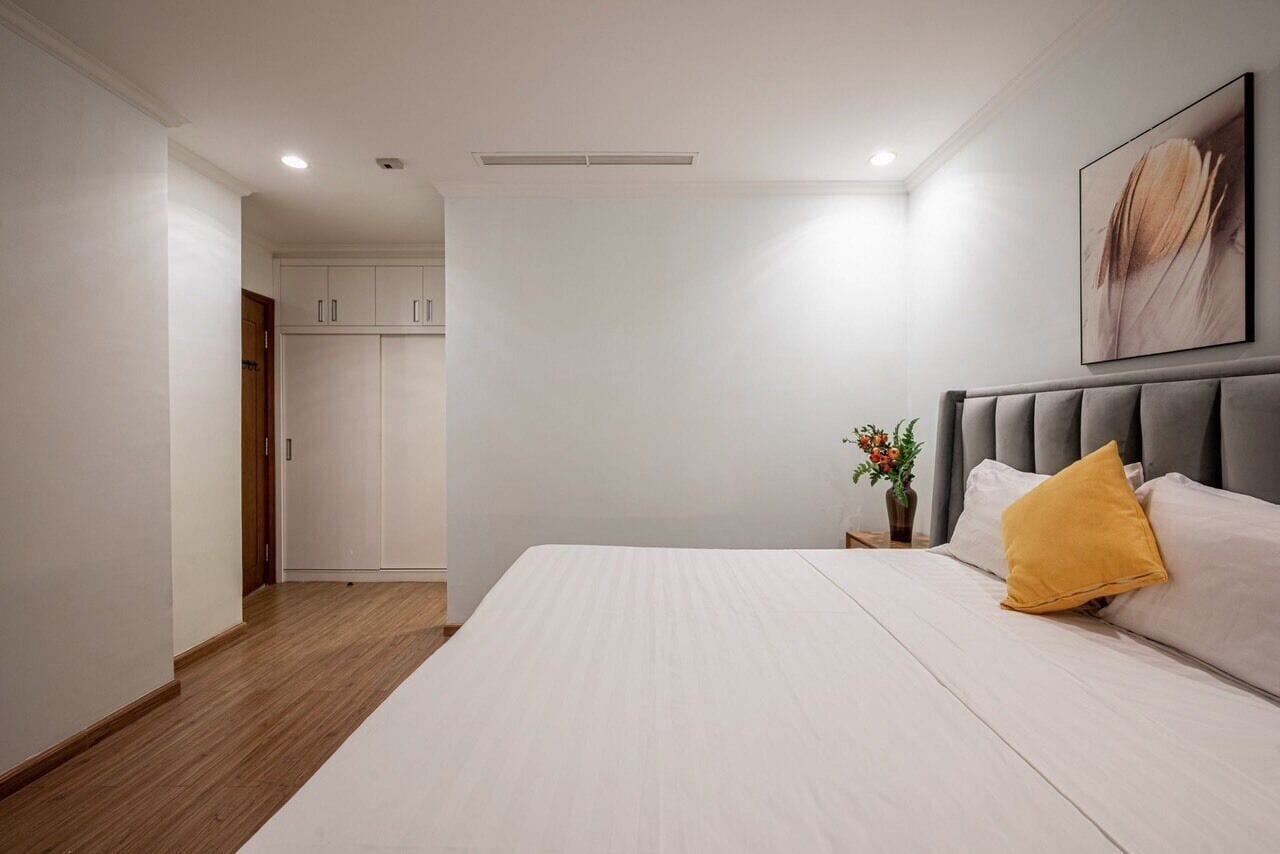 A bedroom with a large bed, a headboard, a nightstand with a vase, and a wardrobe.