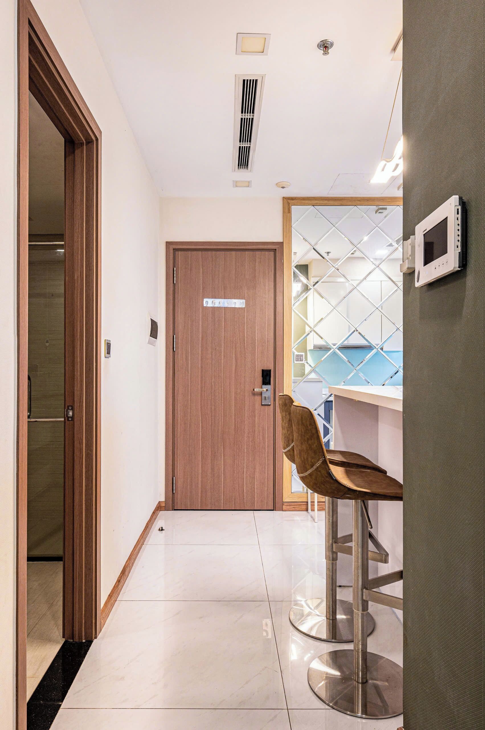 A hallway with a wooden door, a chair, and a counter with a glass partition.