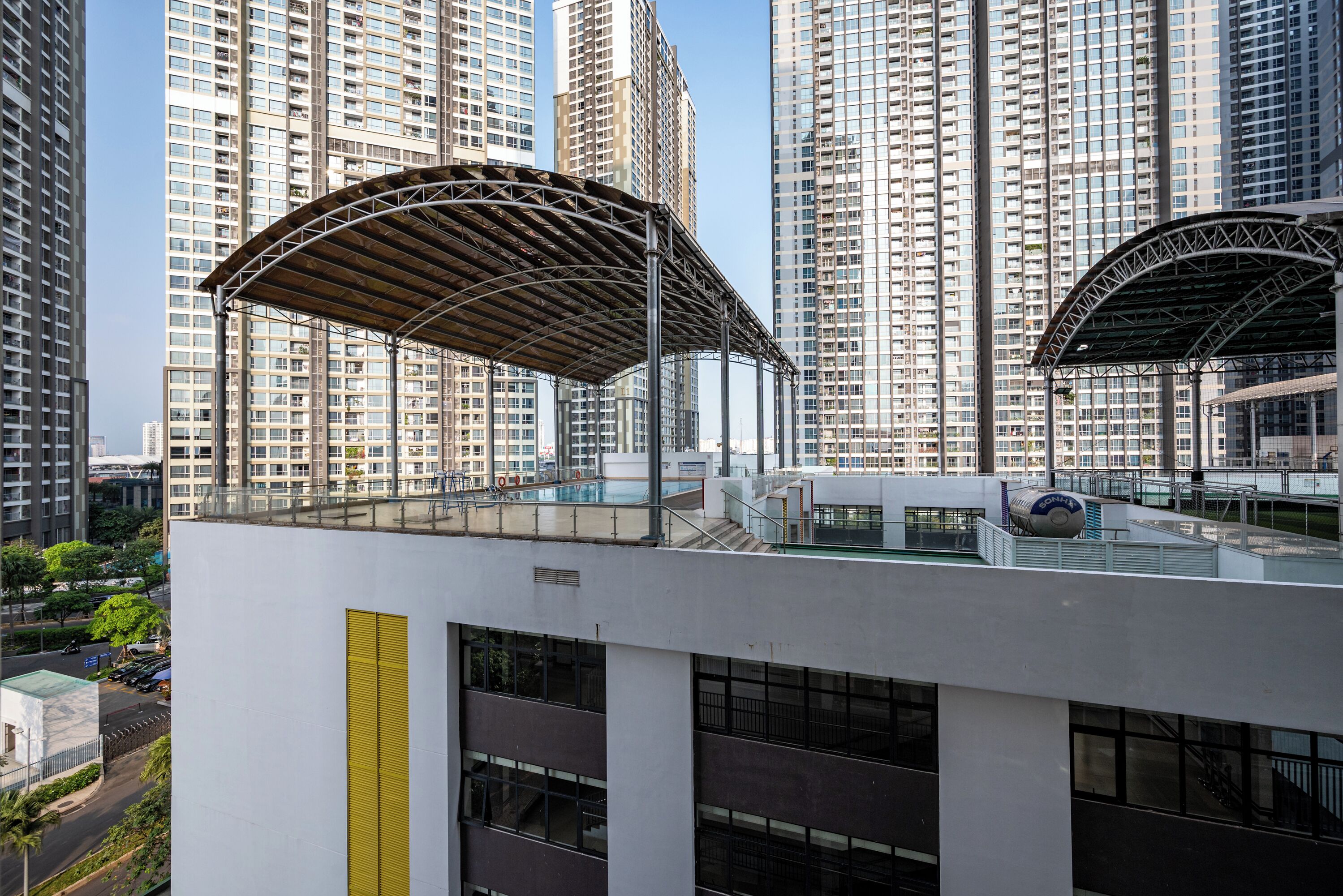 Un edificio moderno con terraza en la azotea, ventanas amplias y una zona cubierta con estructura metálica.