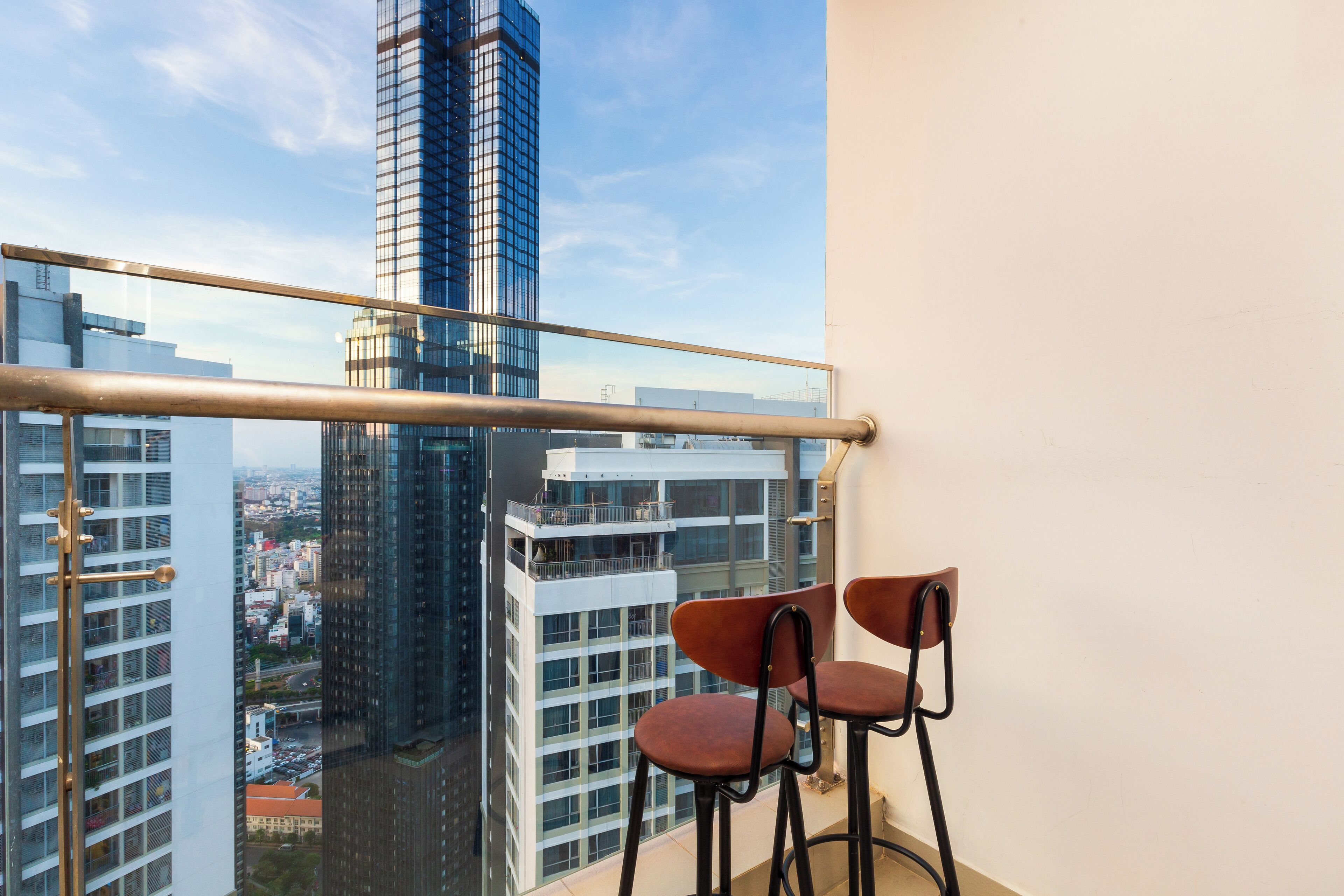 Un balcón con dos sillas, baranda metálica y vistas de edificios altos.
