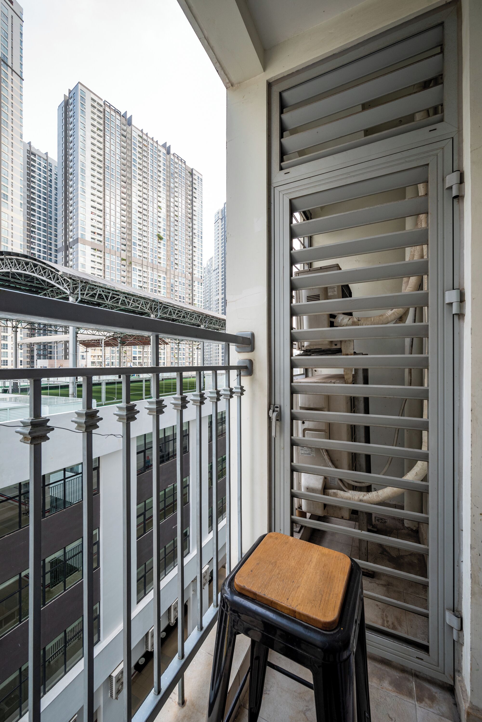 A balcony with a view of high-rise buildings, a metal railing, and a wooden stool.