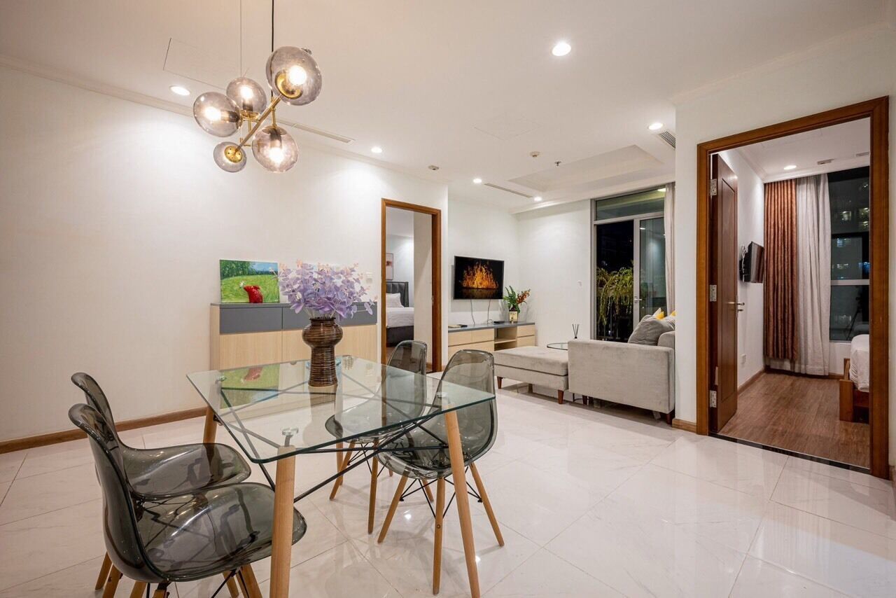 Un espace de salle à manger moderne, avec une table et des chaises en verre, un vase décoratif et un lustre contemporain.