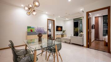 Un espace de salle à manger moderne, avec une table et des chaises en verre, un vase décoratif et un lustre contemporain.