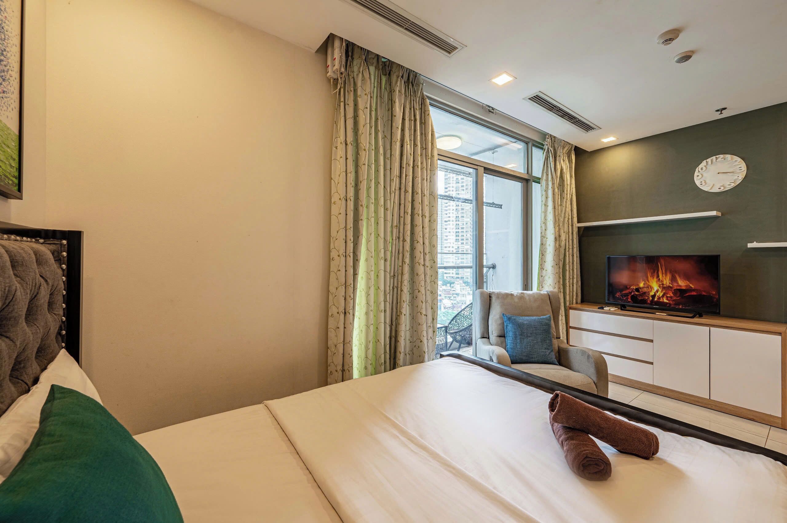 A hotel room with a bed, a television displaying a fire, a sofa, and a window with curtains.