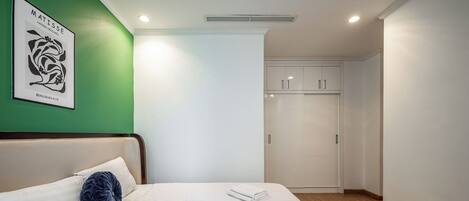 Un letto rifatto con lenzuola bianche e un cuscino decorativo blu, un armadio bianco con uno specchio e una parete verde decorata.