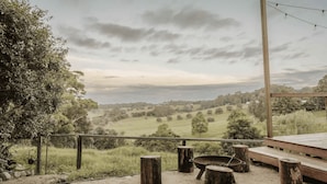 A scenic outdoor area with a wooden deck, a fire pit, and a view of rolling hills and trees.