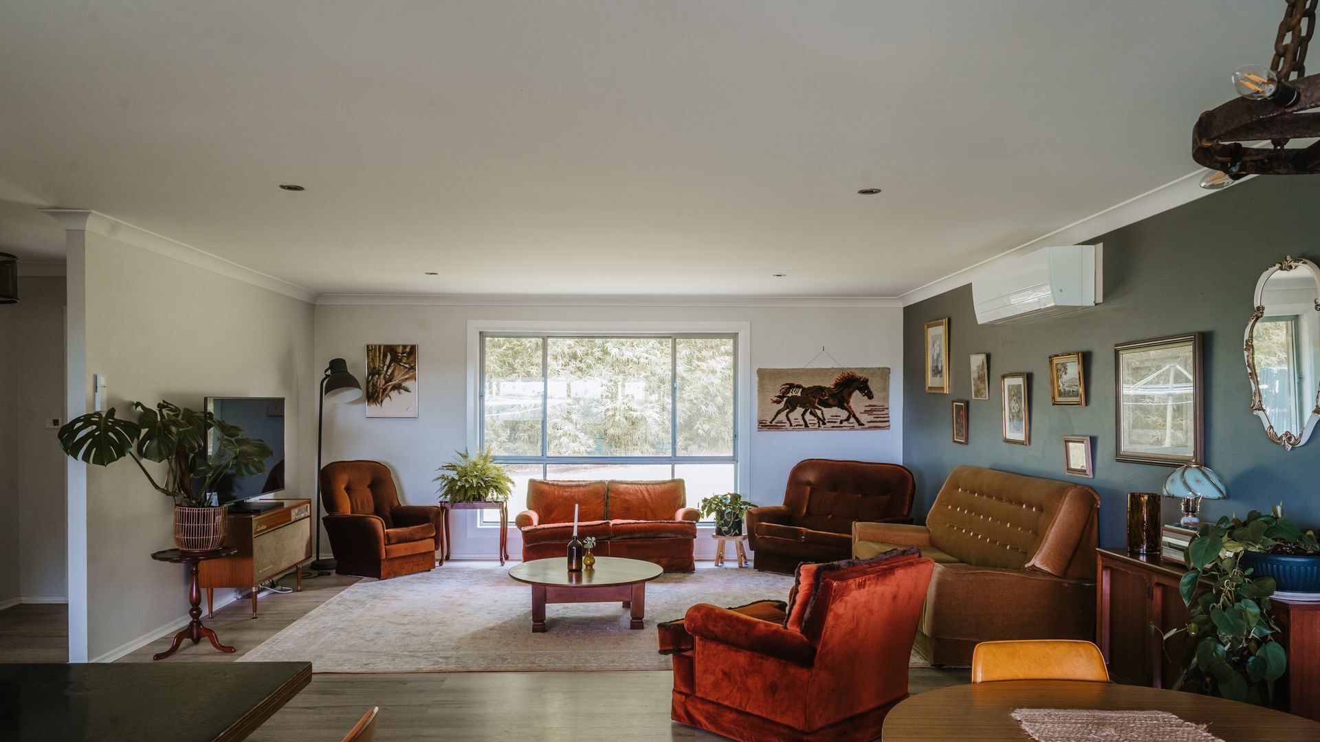 A spacious living room with a large window, multiple seating options, and a variety of wall decorations.