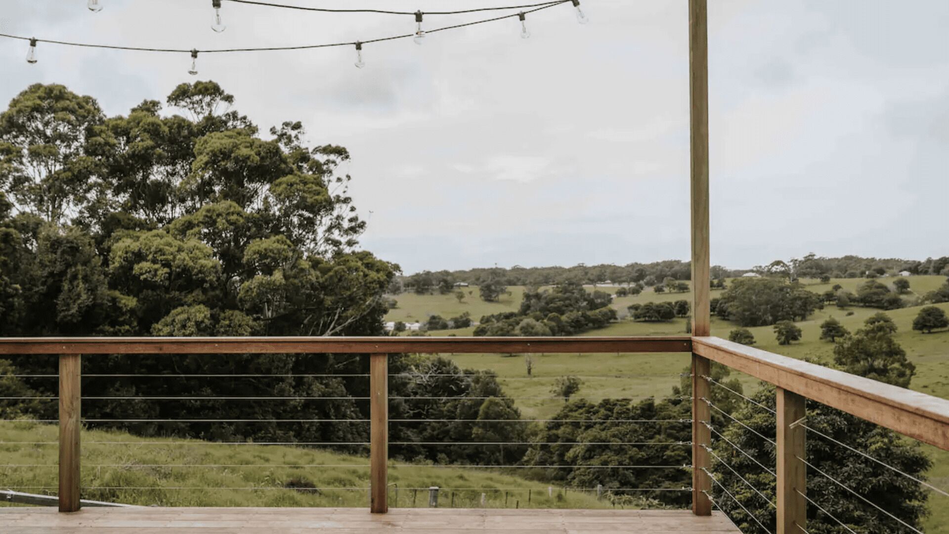 A wooden deck with a metal railing overlooking a grassy landscape with trees.