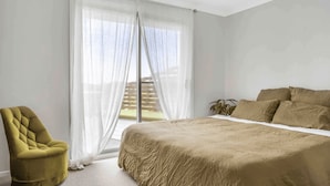 A bedroom with a bed, a chair, and a window with sheer curtains.