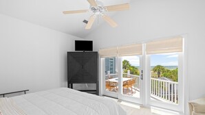 A bedroom with a bed, a TV, a ceiling fan, and a balcony with a view. - 3 Summer Dunes - Renovated Ocean View Beach House! (Isle of Palms)