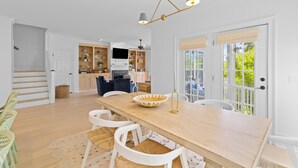 A spacious dining area with a wooden table, white chairs, and a decorative bowl centerpiece. - 3 Summer Dunes - Renovated Ocean View Beach House! (Isle of Palms)