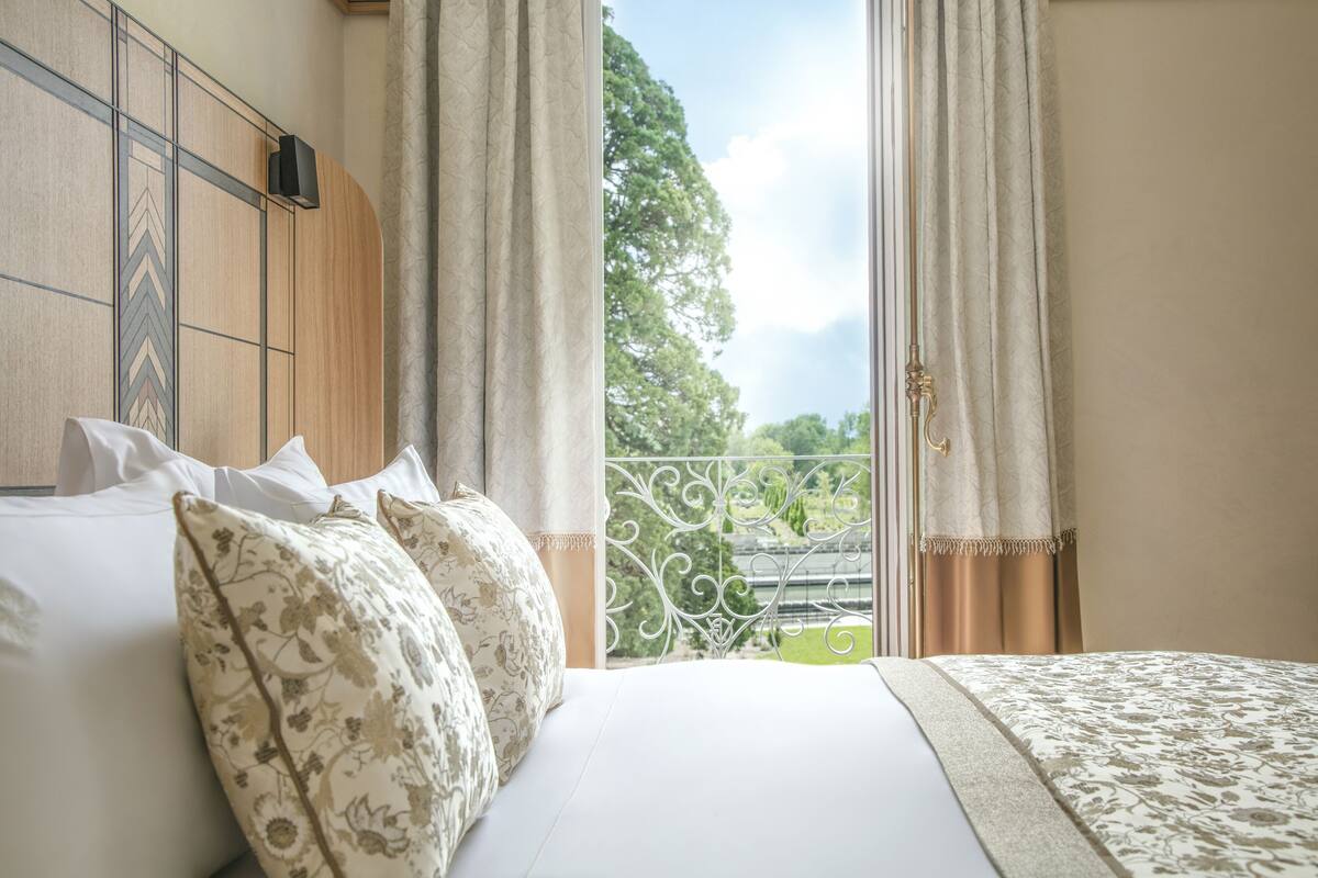 Une chambre d’hôtel avec un lit, une vue sur la verdure et un balcon doté d’une balustrade.