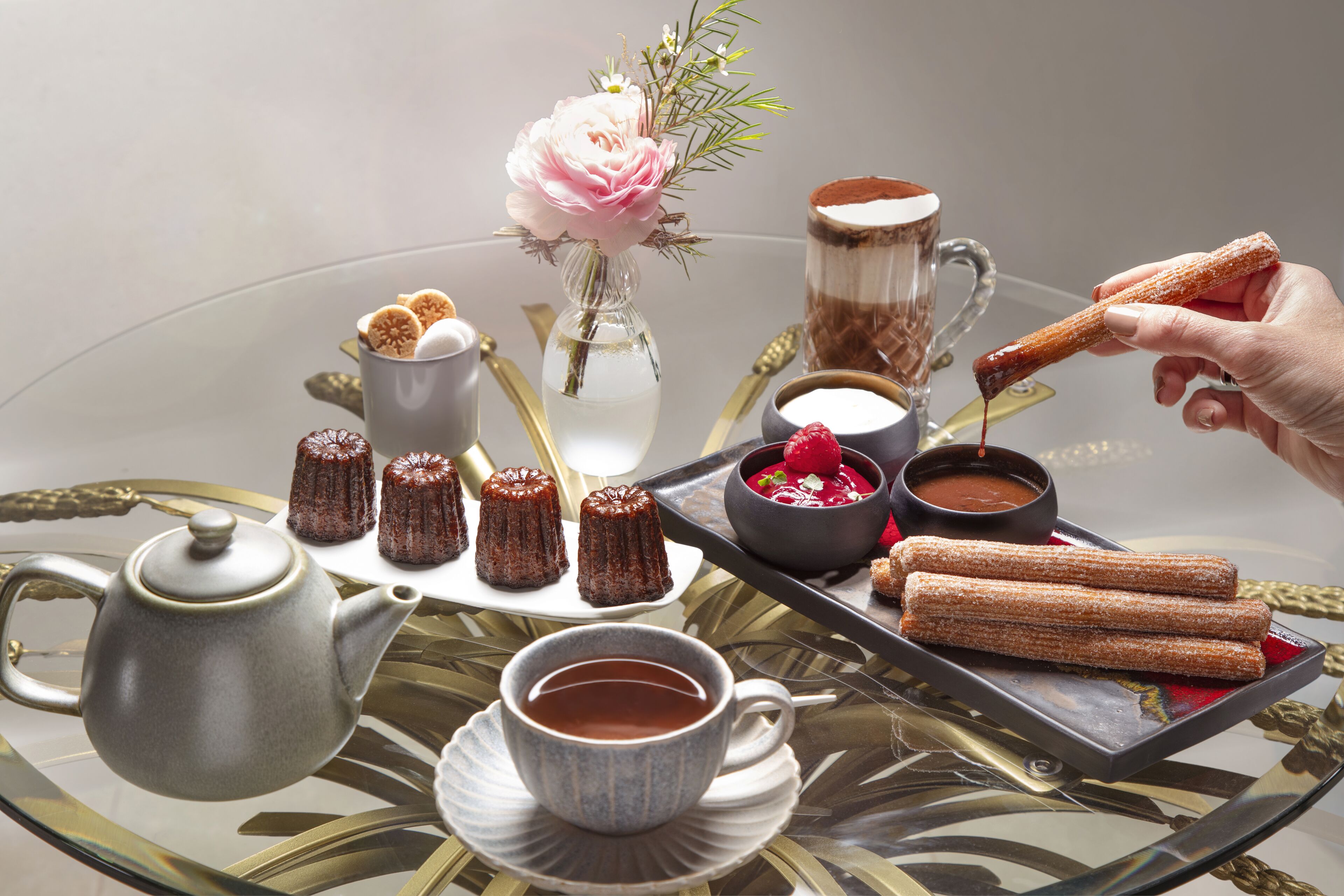 Une table mise avec une théière, des tasses, un vase de fleurs et des churros.