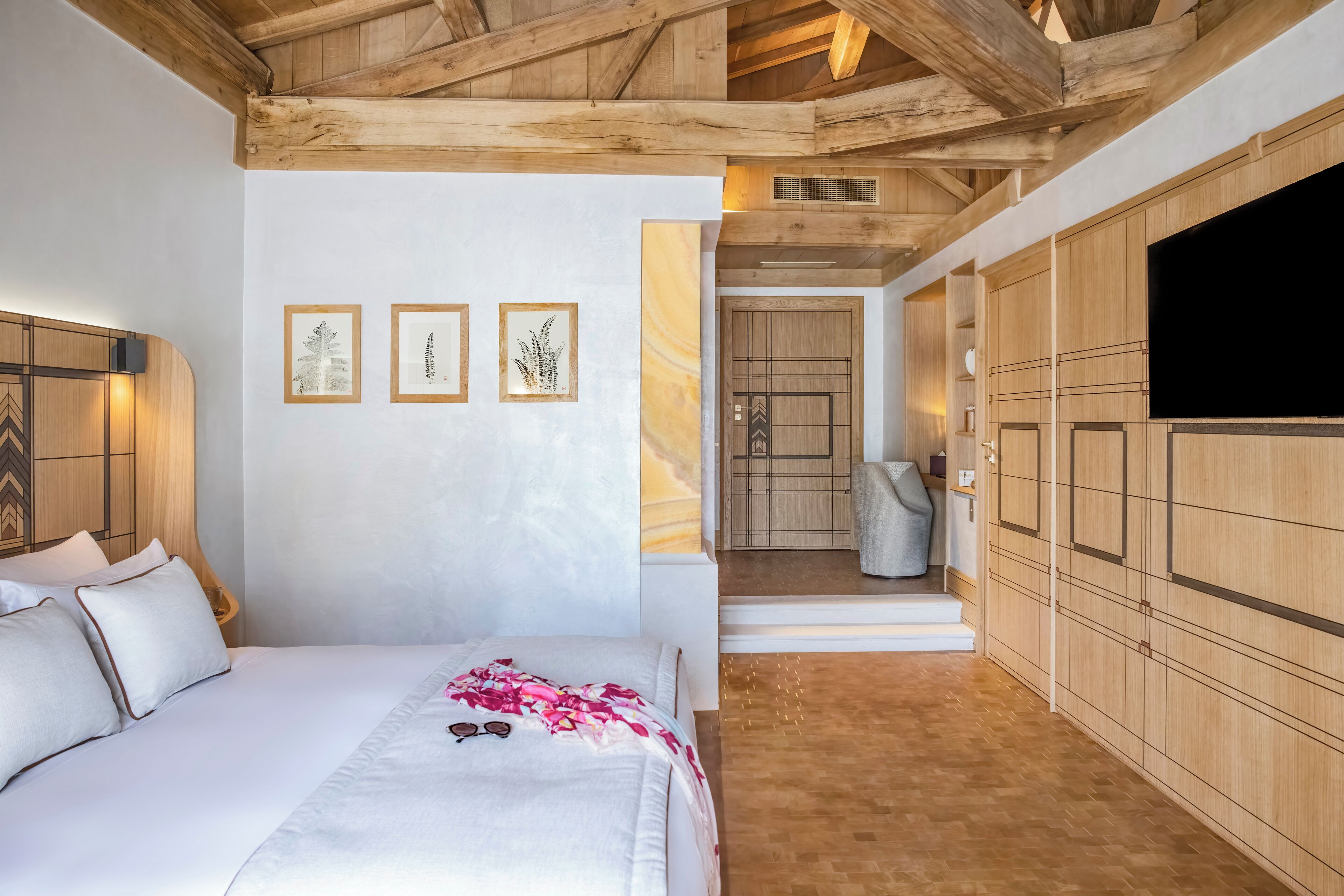 A bedroom with a bed, a wooden wardrobe, and framed artwork on the wall.