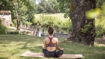 A person sitting on a yoga mat outdoors with a tree and a body of water in the background.