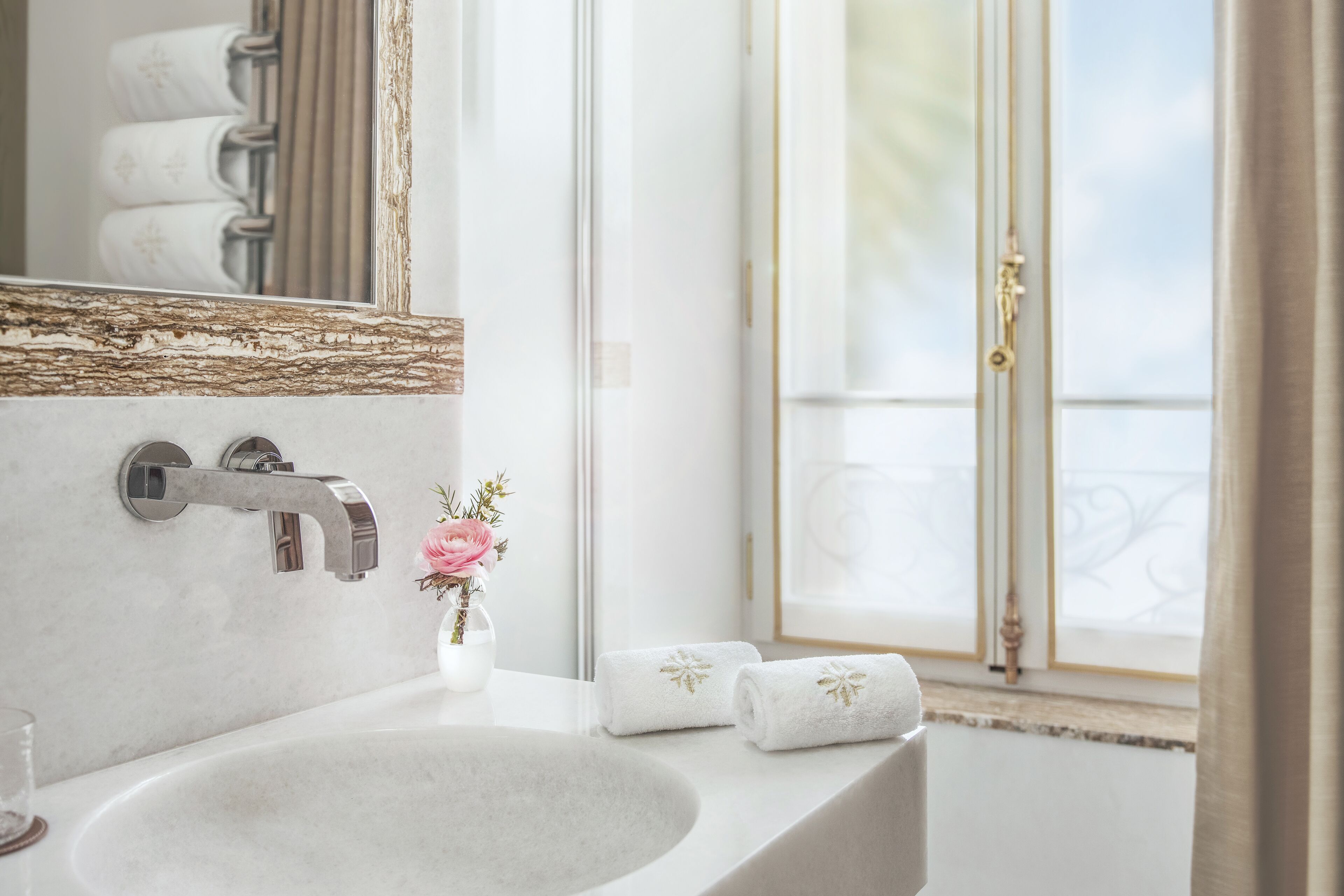 A bathroom with a marble sink, a modern faucet, and a large mirror. There are towels on the counter and a window with a view of the outdoors.
