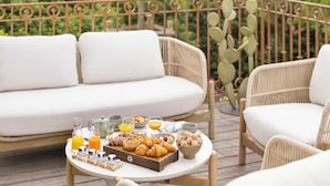 Een ontbijt opstelling op een terras met rieten meubels, een dienblad vol gebak en diverse drankjes.