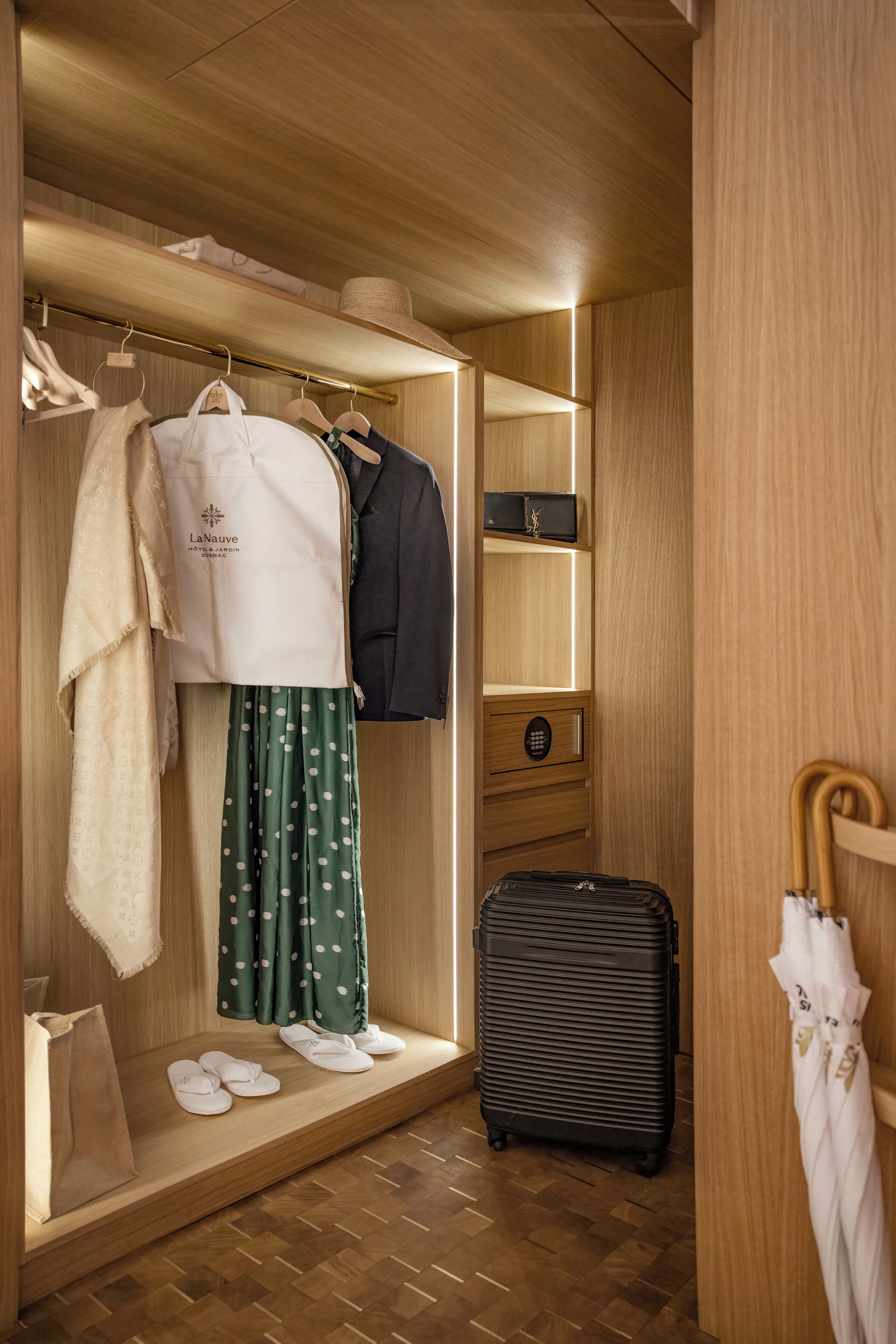 Ein Hotelzimmer mit einem Holzschrank, einem Koffer und einem Kleiderständer mit Kleidung und einem Hut.